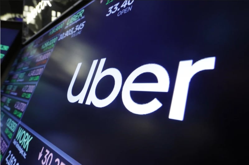 The logo for Uber appears above a trading post on the floor of the New York Stock Exchange, Aug. 16, 2019. Uber is shutting down alcohol delivery app Drizly, the company confirmed this week, just under three years after acquiring the platform for $1.1 billion. Drizly will officially shut down at the end of March, Uber told The Associated Press (AP Photo/Richard Drew, File).
