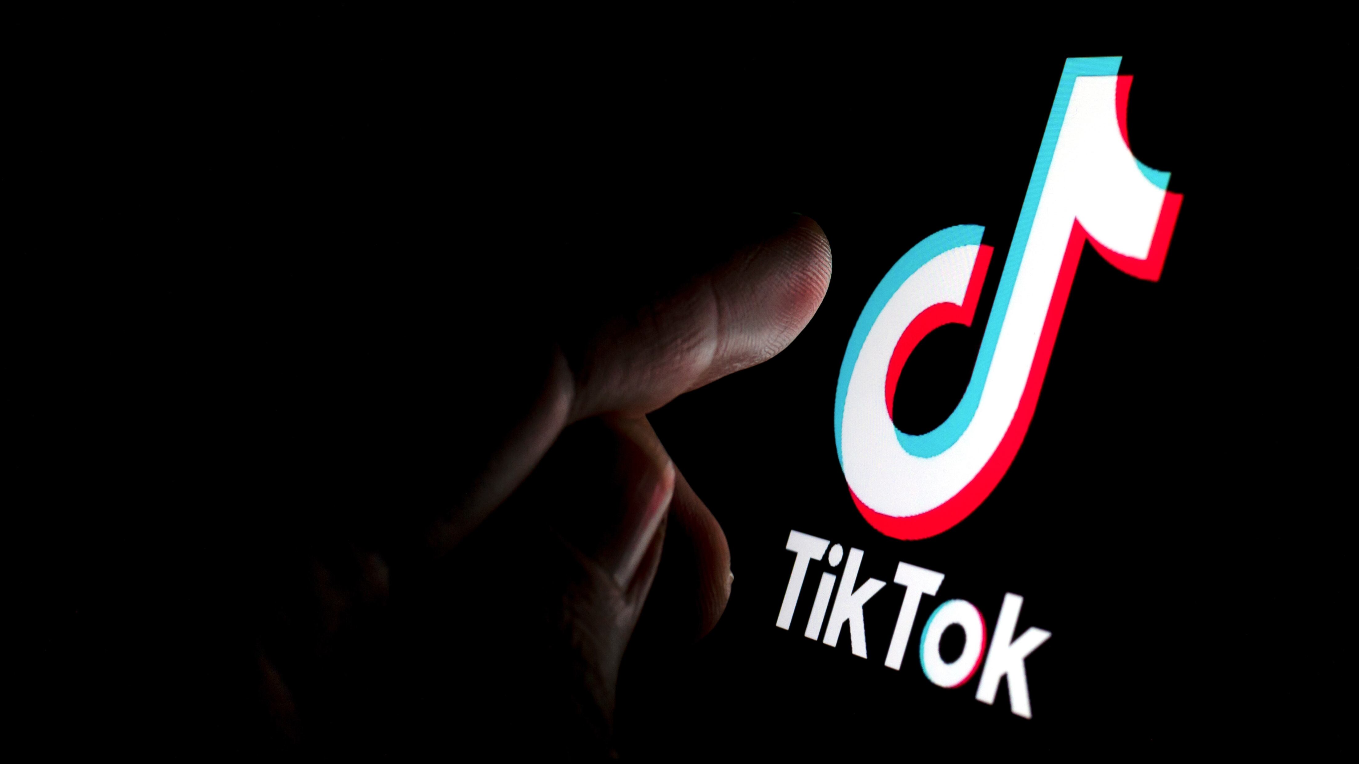 TikTok app logo on the screen and a finger about to touch it.