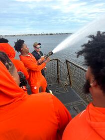 Members of the Clemson football team try out the high pressure fire hose onboard Naval Station Mayport-based USS Jason Dunham.