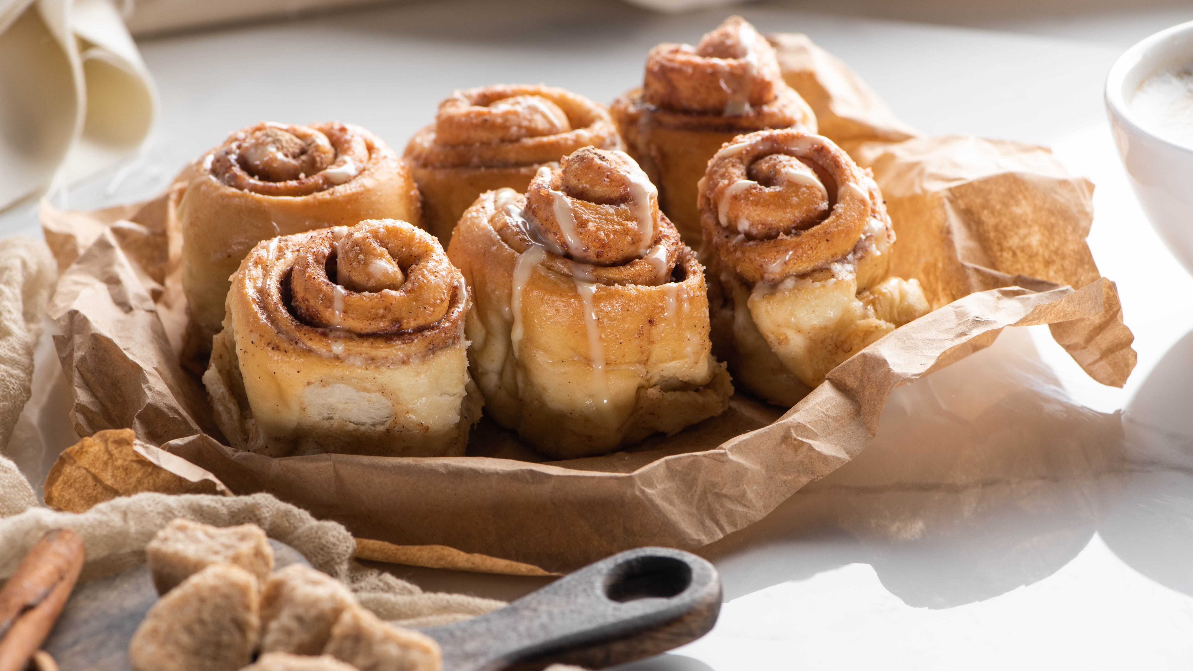 fresh homemade cinnamon rolls near cutting board with brown sugar and cinnamon sticks