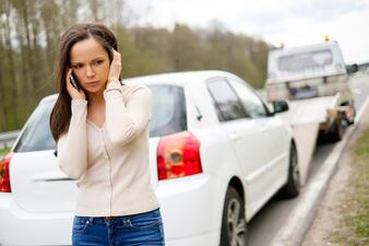 woman with broken car on side of road via dreamstime